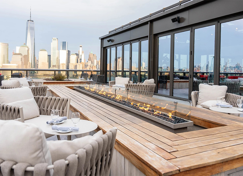 a fire pit on a table with chairs and a city skyline in the background