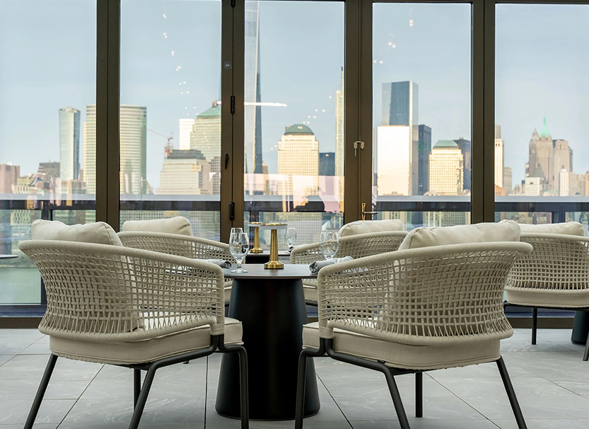 a table with chairs and a glass door with a city view in the background