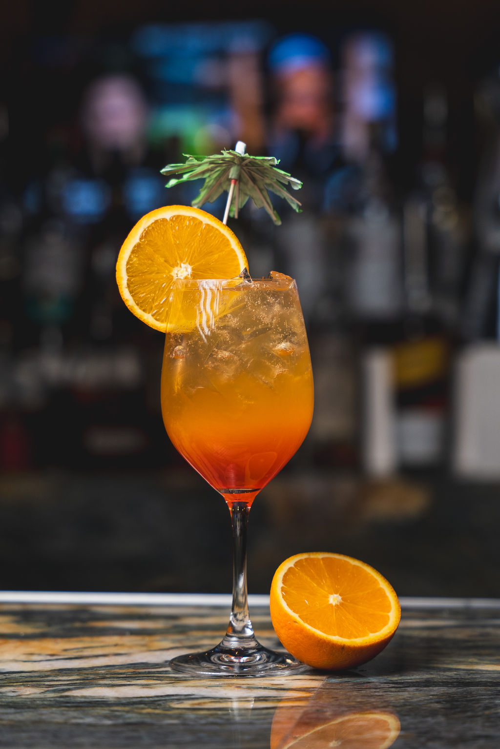 a glass with orange and yellow liquid and an umbrella on top