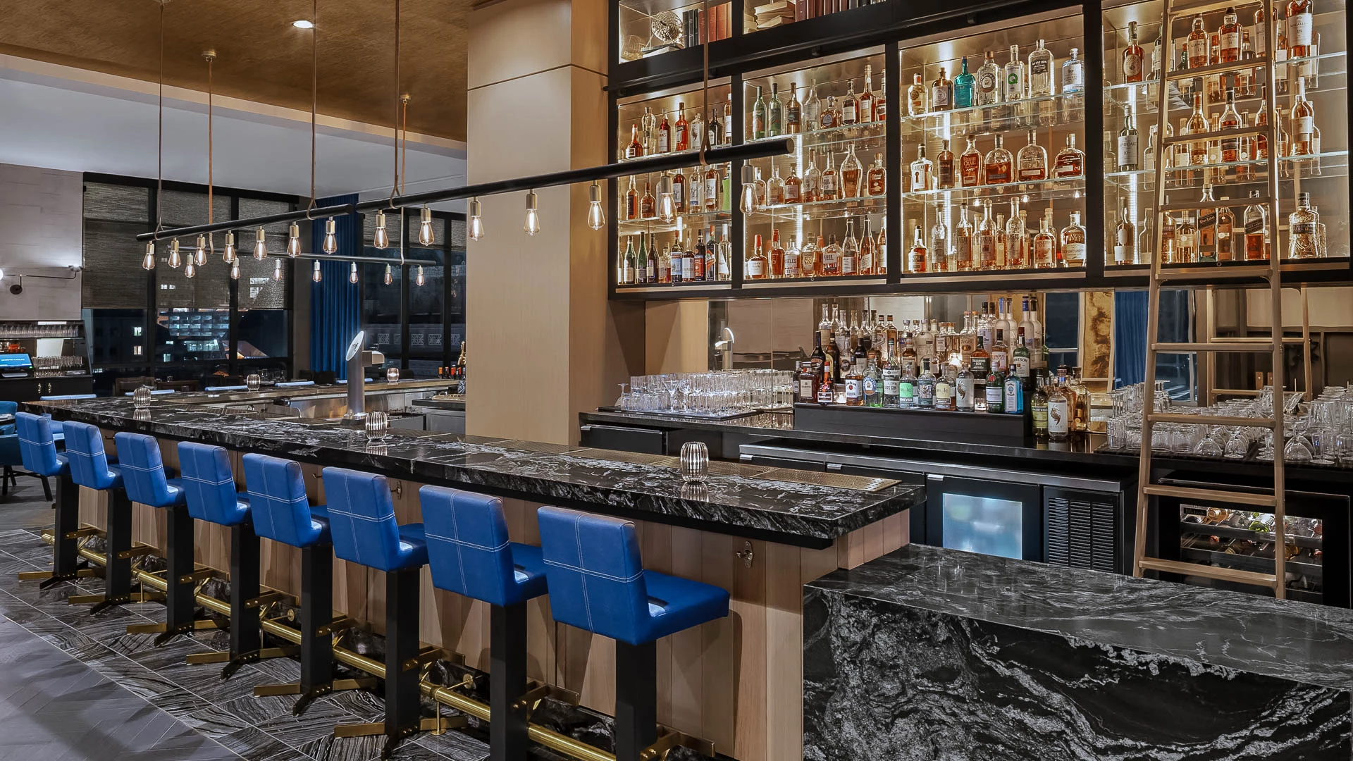 a bar with shelves of liquor and blue chairs