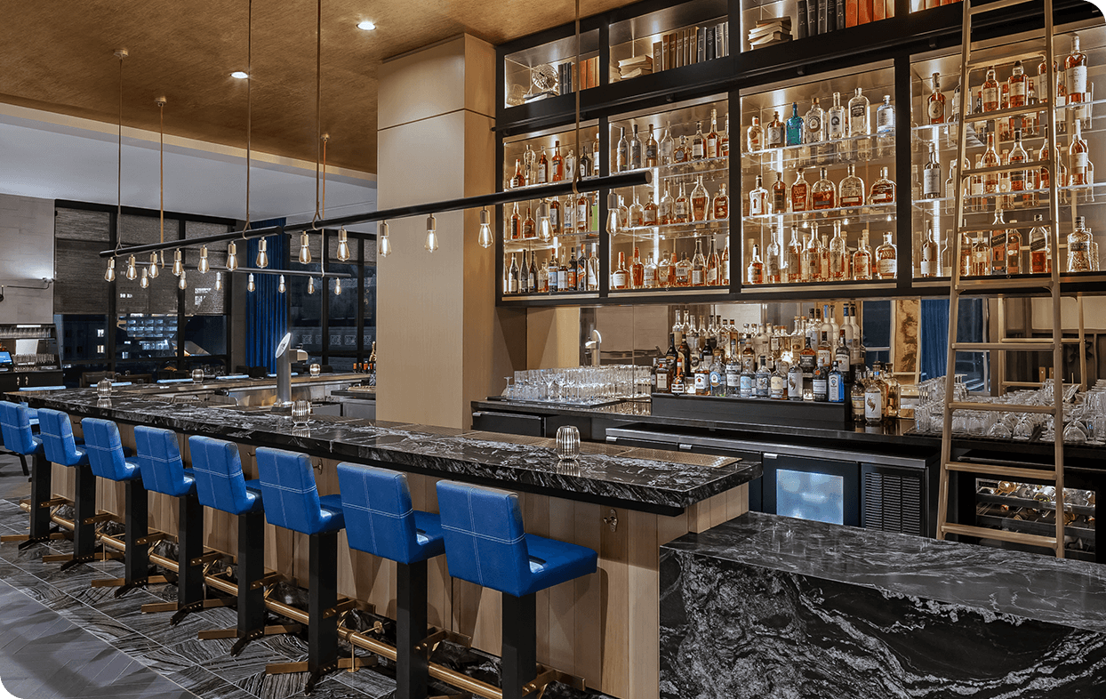 a bar with shelves of liquor and blue chairs