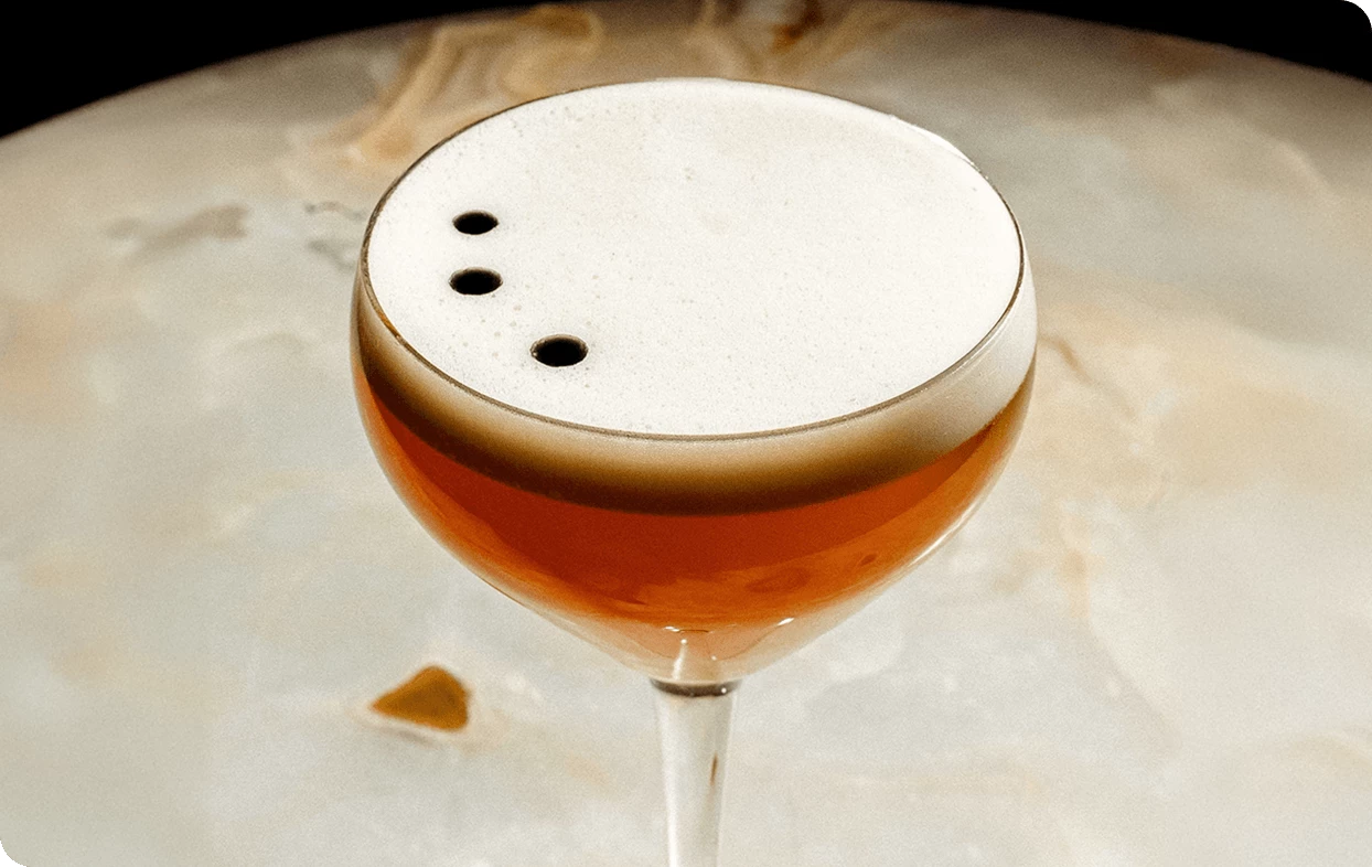 a glass with a brown liquid and three dots on top