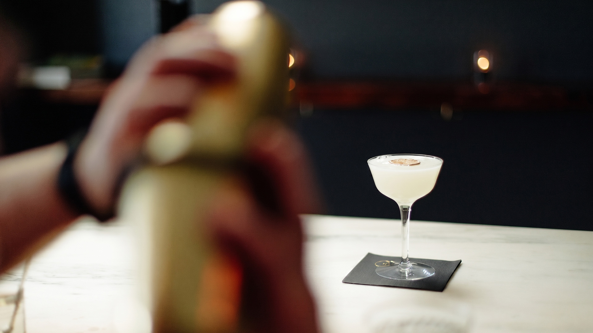 a hand holding a shaker in front of a glass of liquid