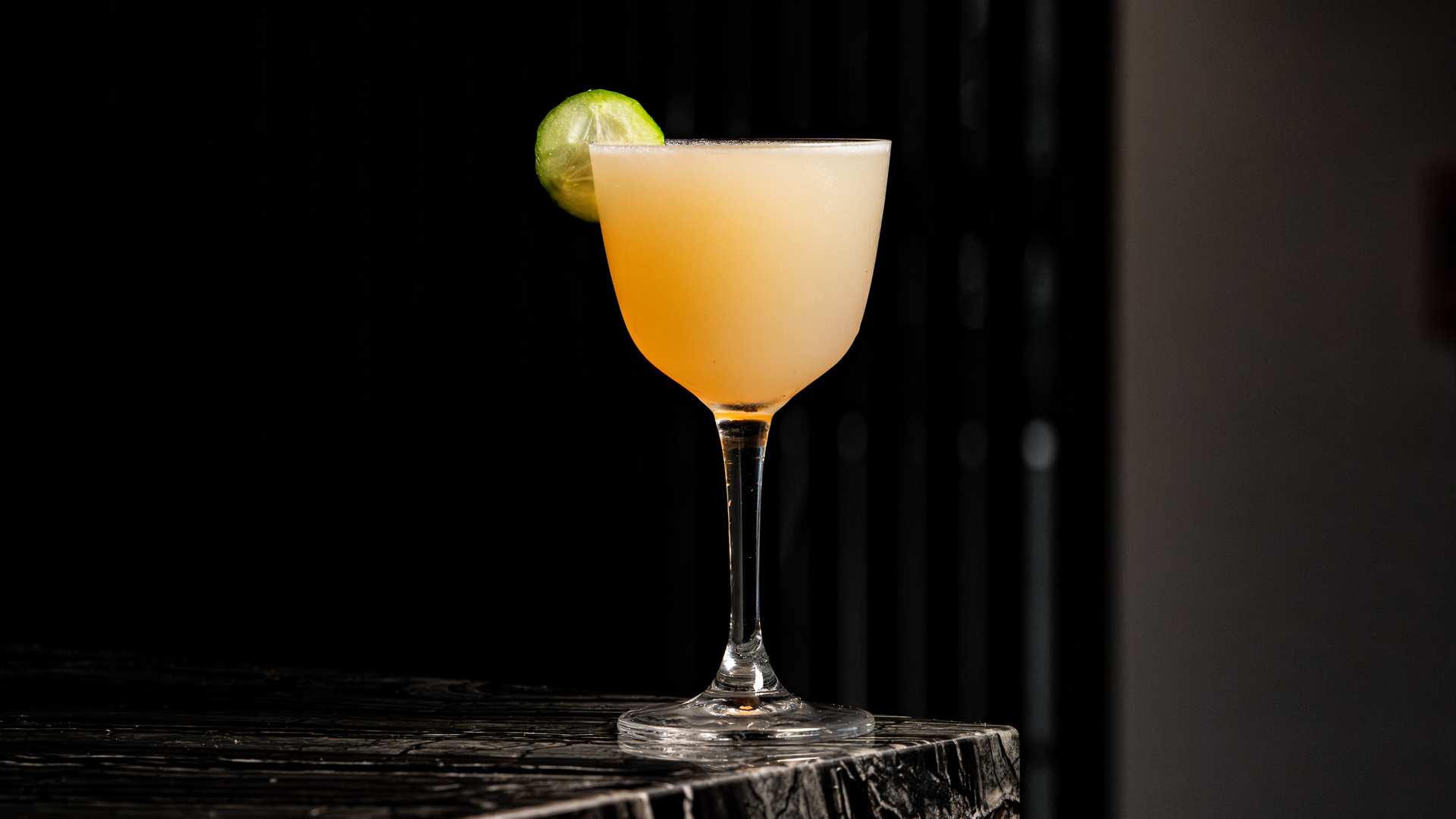 a glass of yellow liquid with a lime slice on top of it