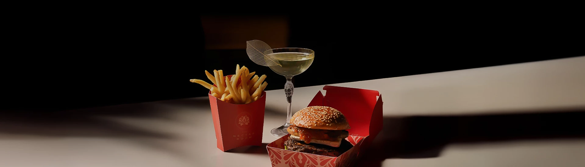 a burger and fries in a red box next to a glass of wine