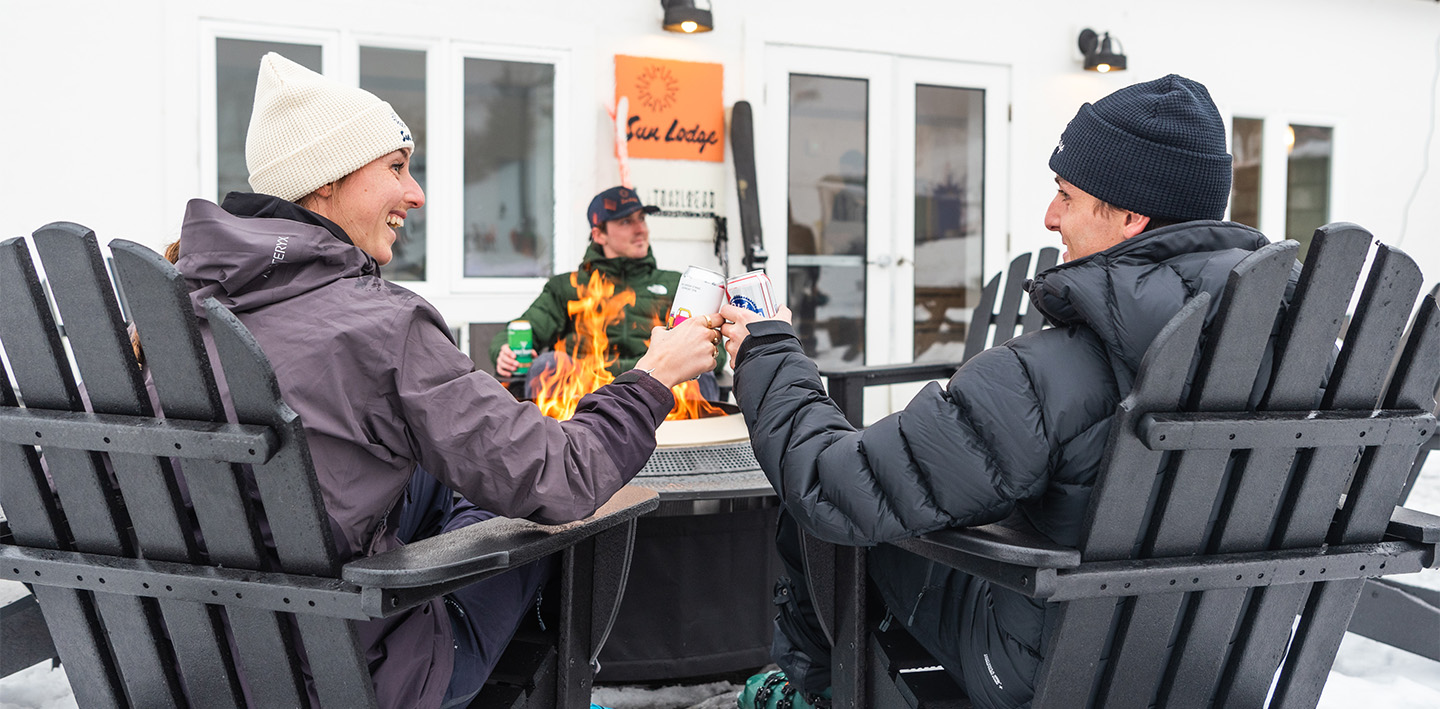a couple of people sitting by a fire with drinks