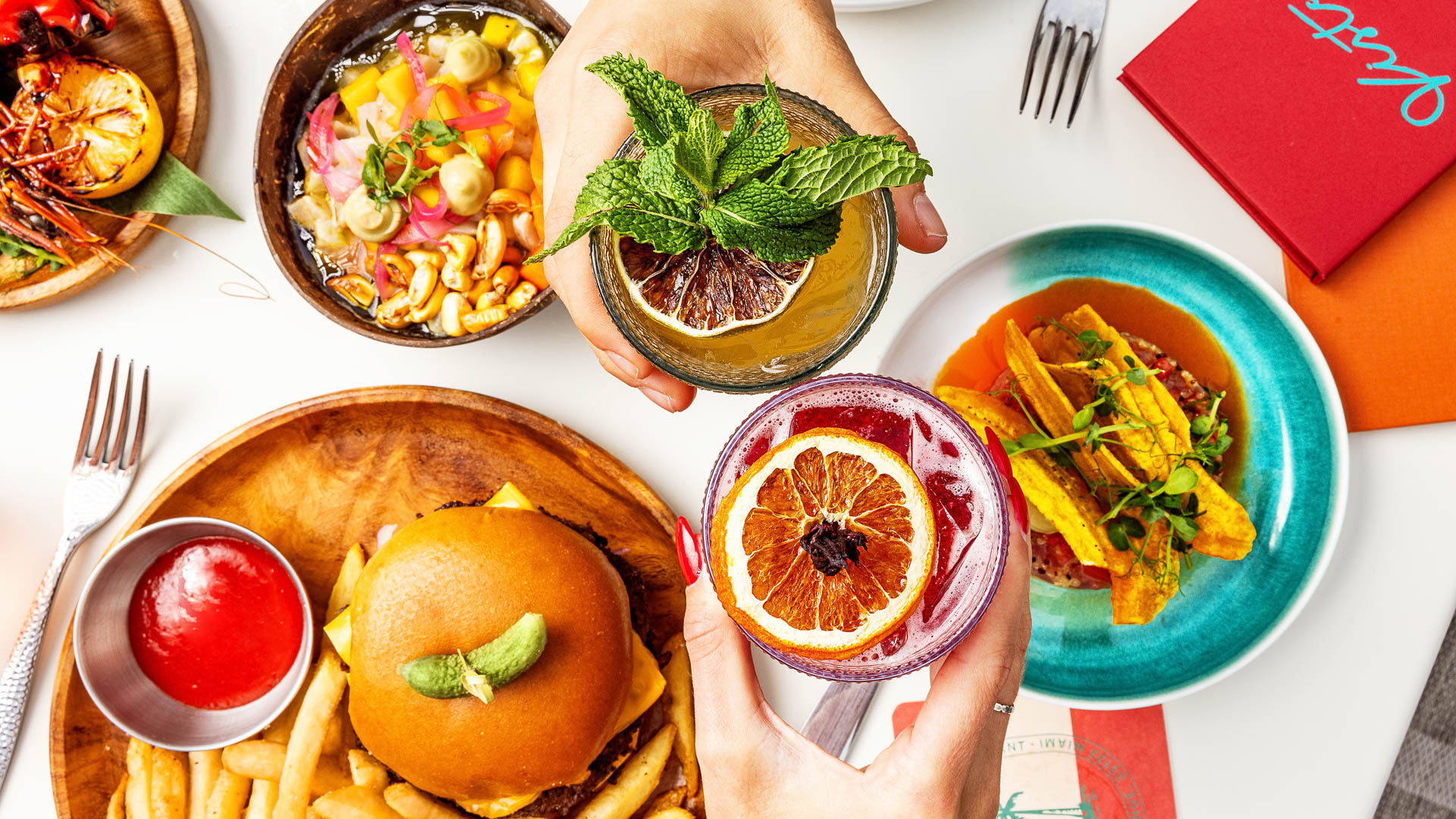a group of hands holding drinks with food on a table