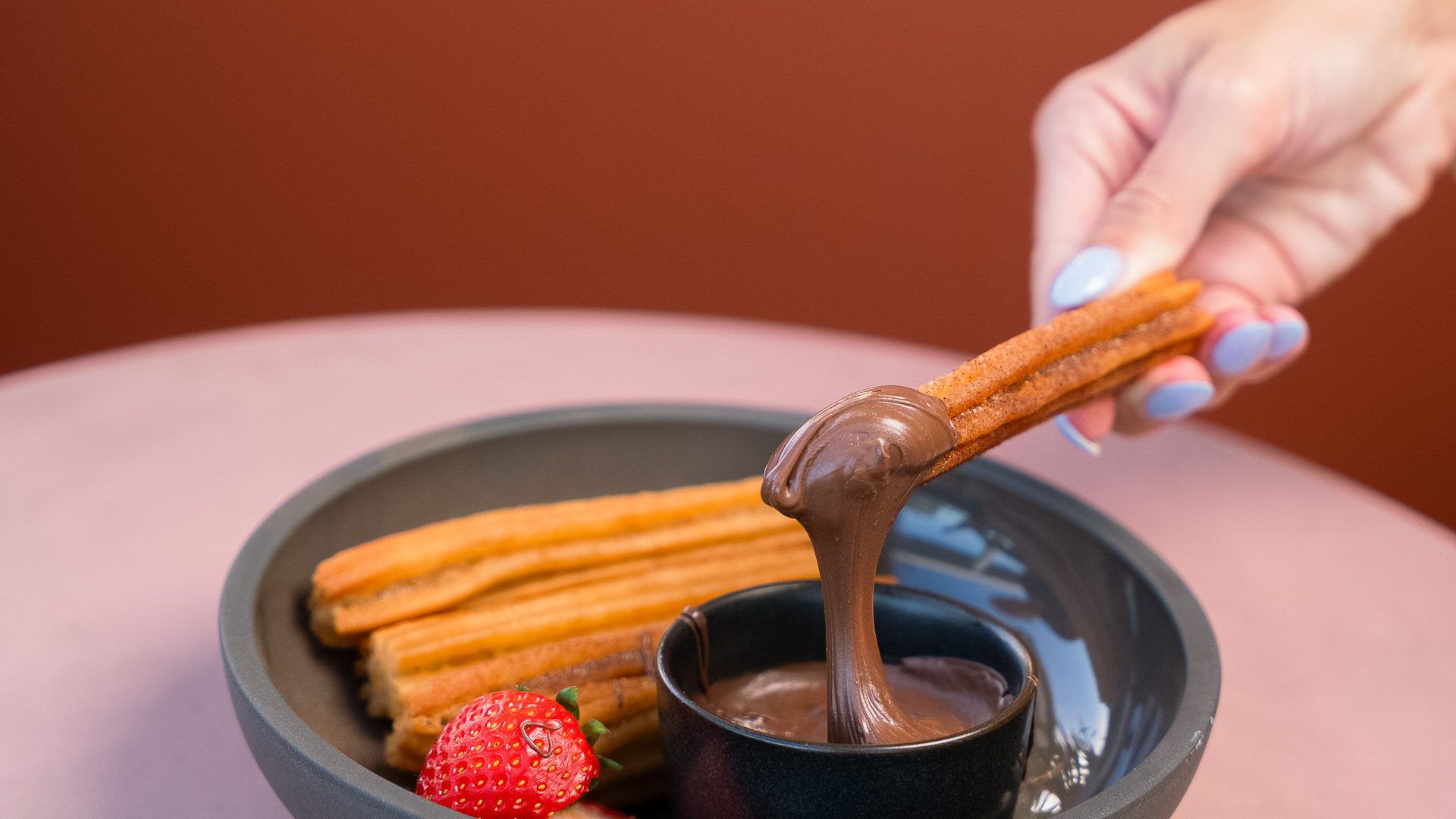 a person dipping chocolate into a bowl of churros
