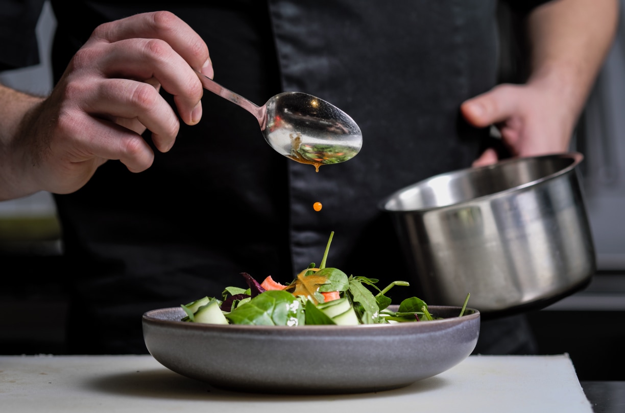 a person pouring sauce over a bowl of salad