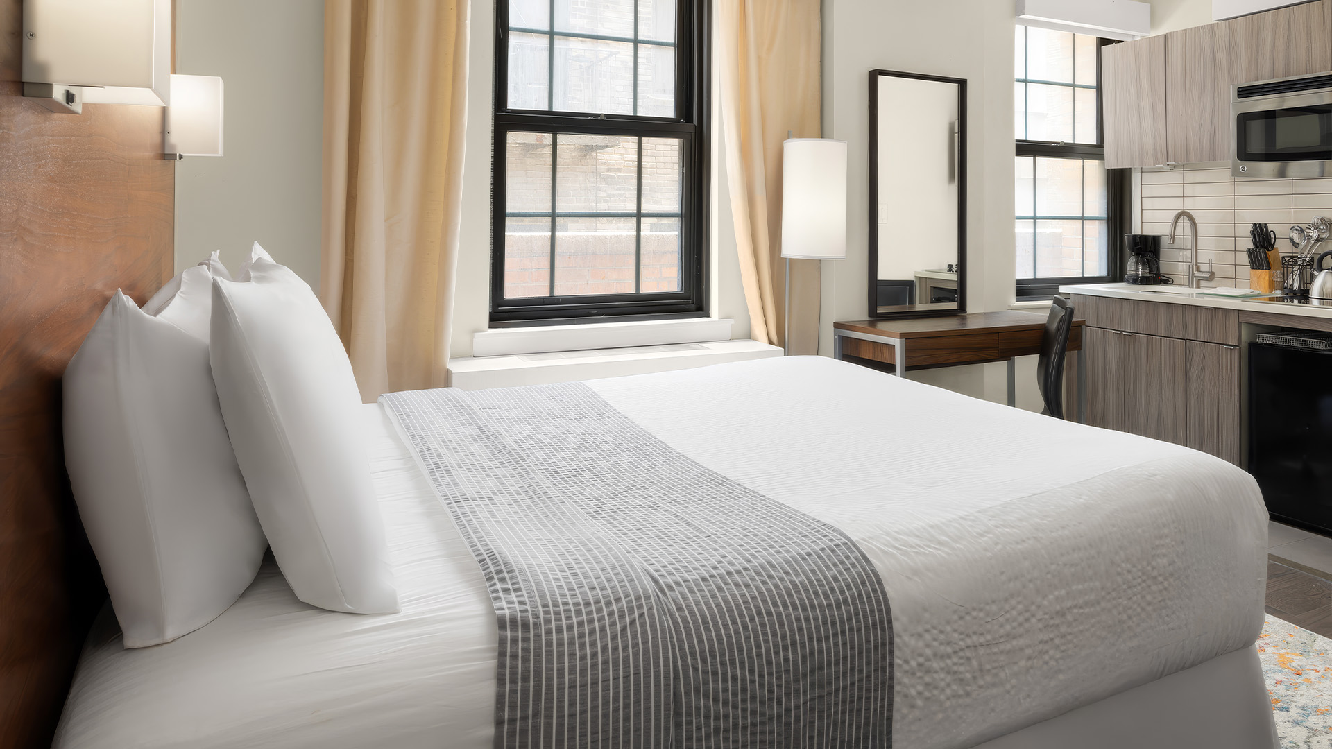 a bed with a white blanket and a table with a mirror and a desk