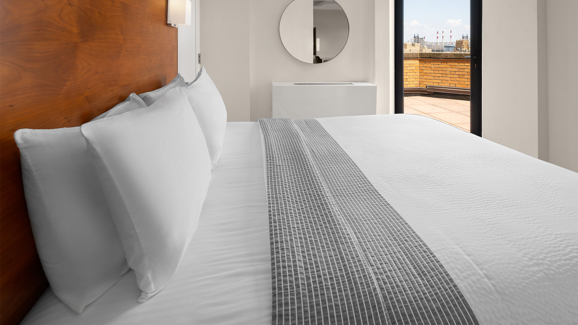 a bed with white sheets and a round mirror