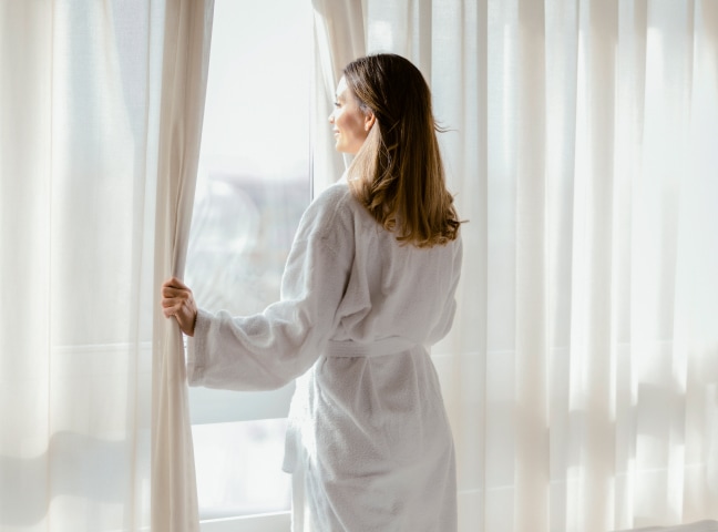 a woman in a white robe opening curtains