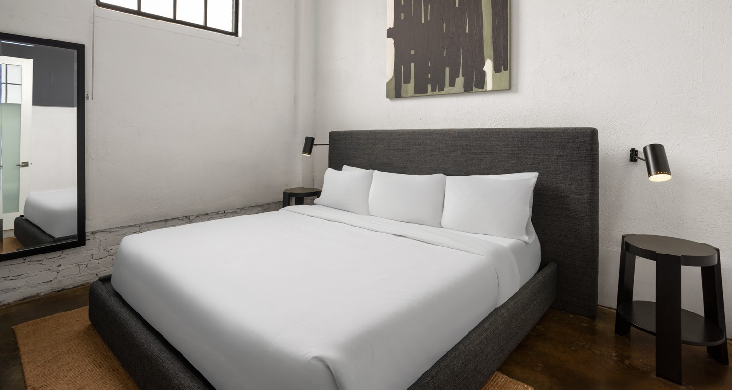 a bed with white sheets and a black and white painting on the wall