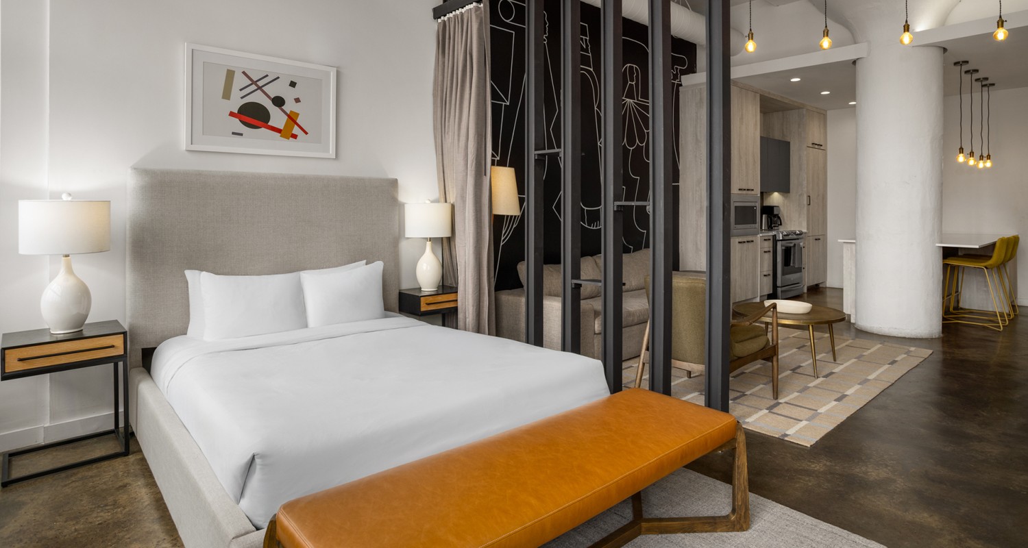 a bed with a leather bench in a room with a kitchen and a bar