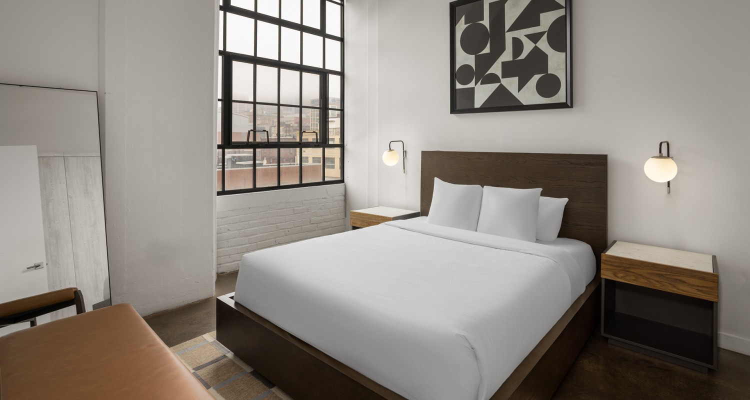 a bed with white sheets and pillows in a room with a window