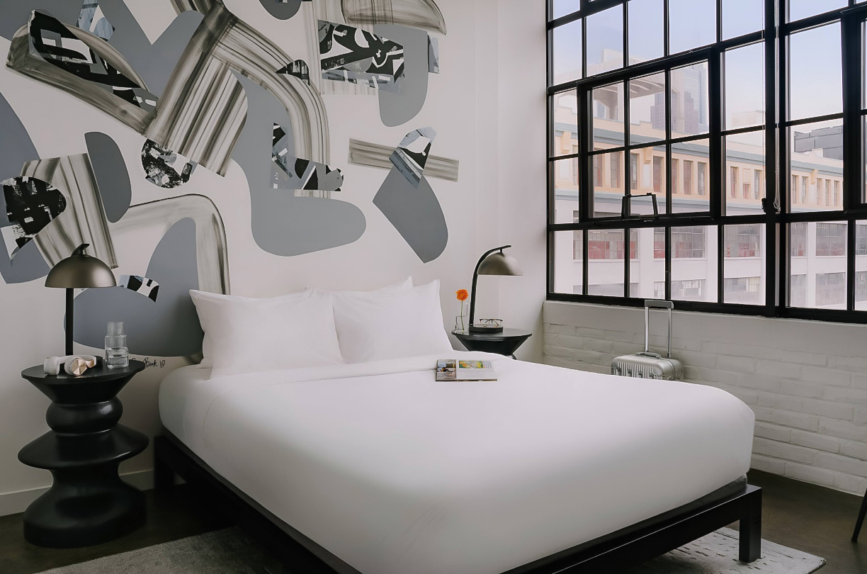 a bed with white sheets and a lamp in a room with windows