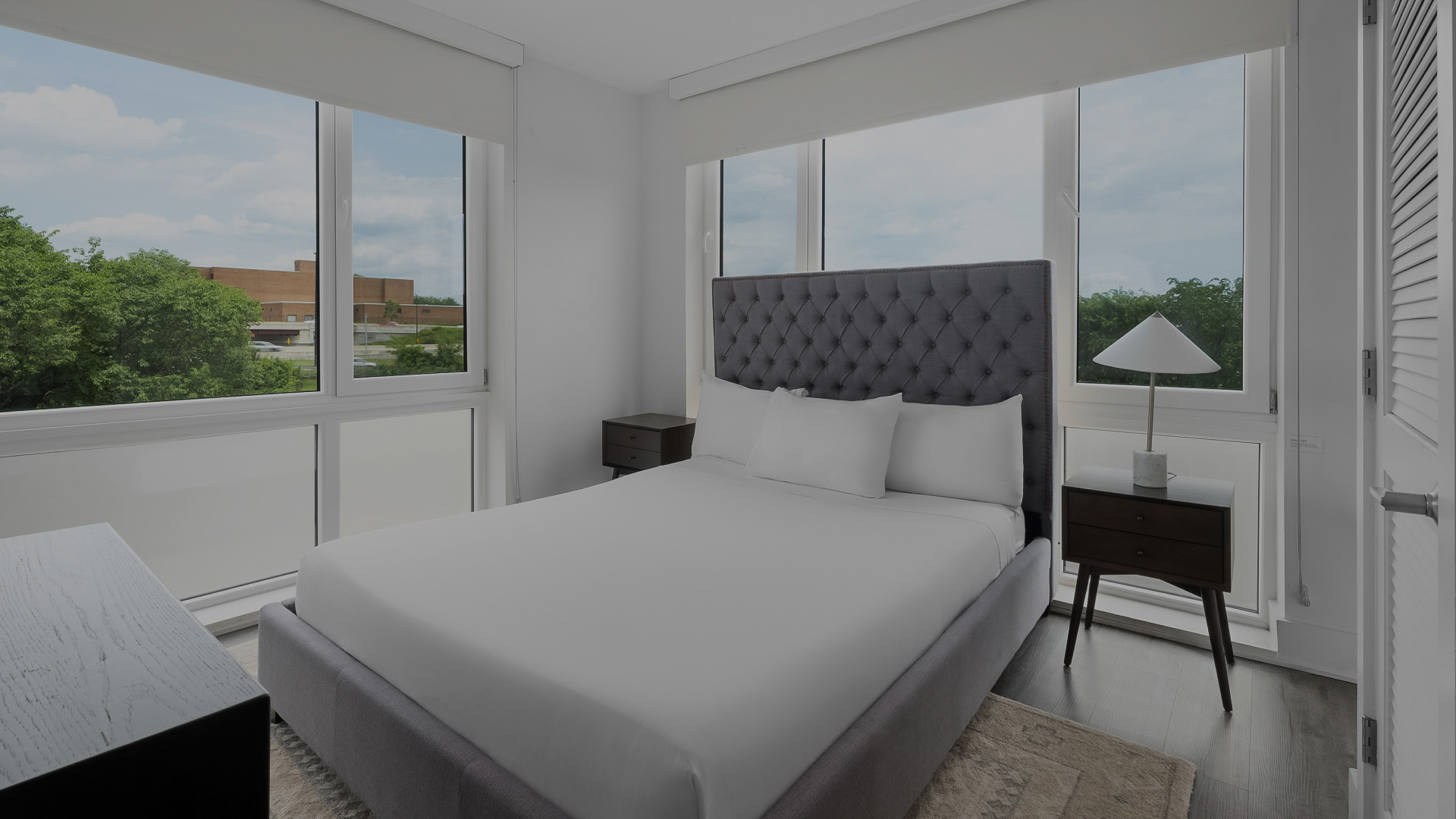 a bed with white sheets and pillows in a room with windows