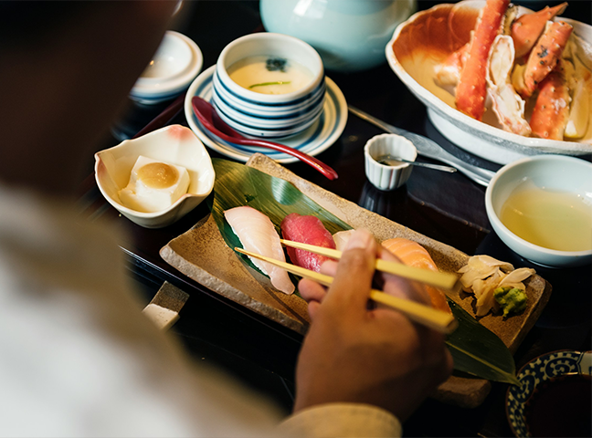 a person holding chopsticks to a plate of sushi
