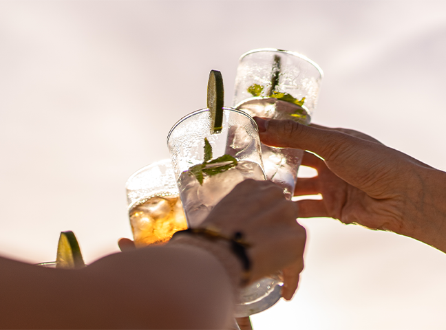 a group of hands holding glasses with ice and lime slices