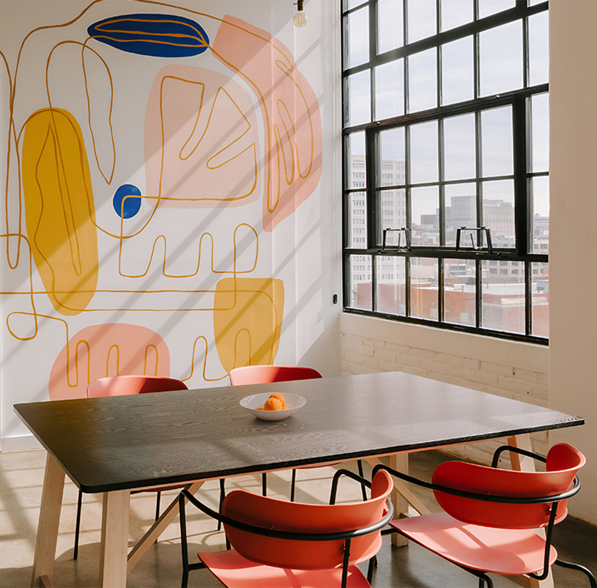 a table and chairs in a room with windows and a wall with a painting