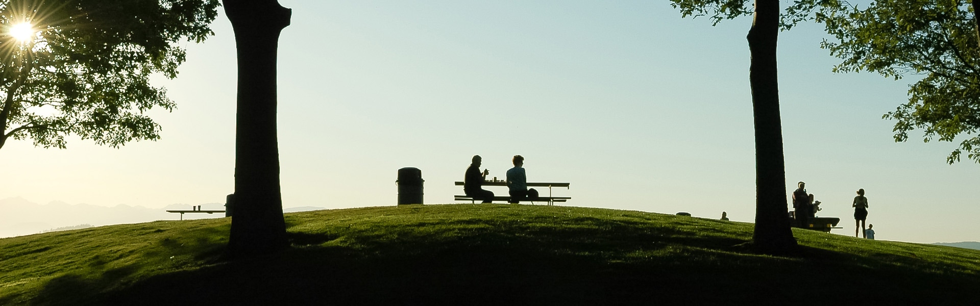 a couple of people sitting on a bench on a grassy hill
