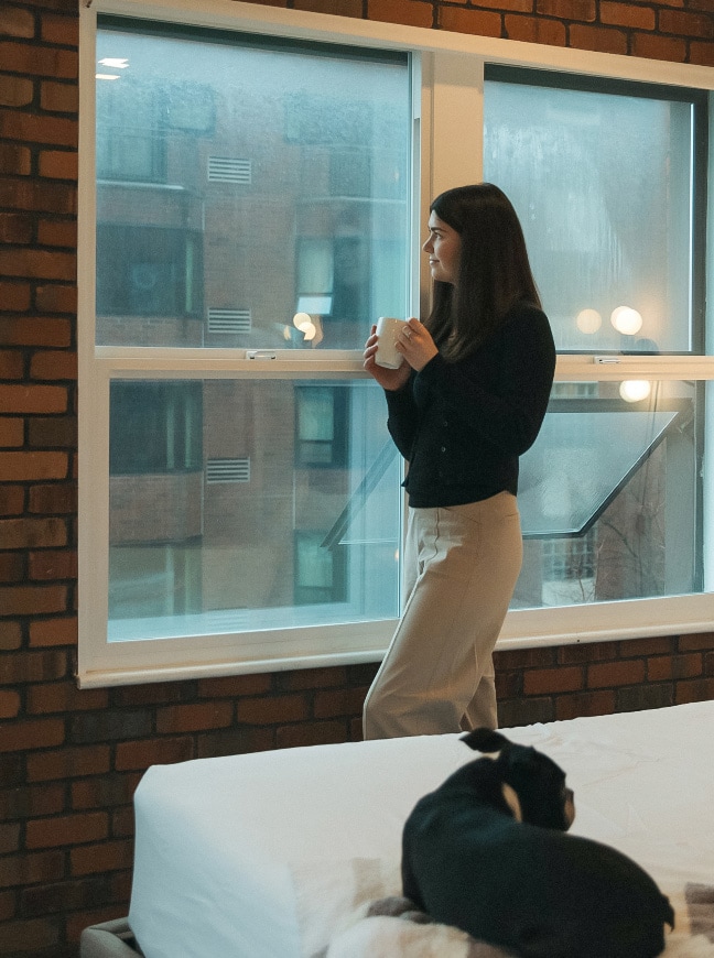 a woman holding a cup looking out a window