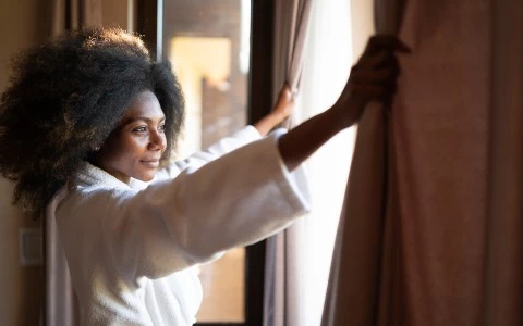 a woman opening curtains in a room
