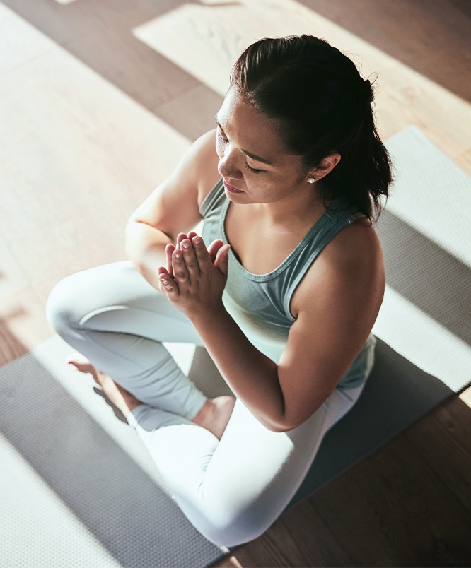 a woman sitting on a yoga mat and holding her hands together