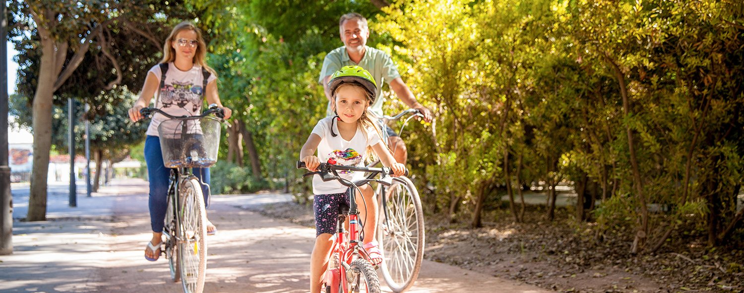 Couple & daughter riding bikes on path surrounded by trees 