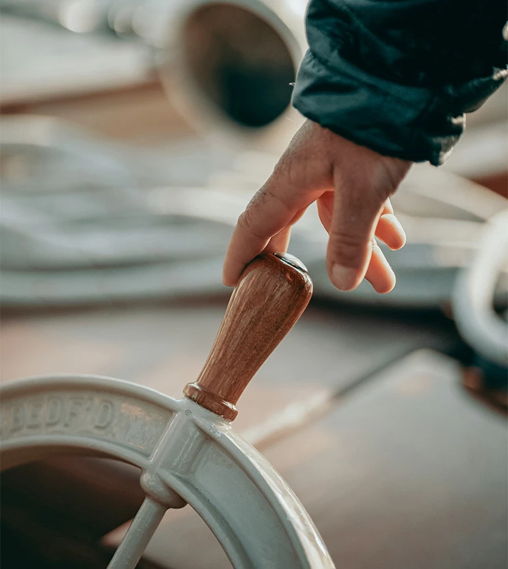 a hand holding a wooden handle on a white ship steering wheel