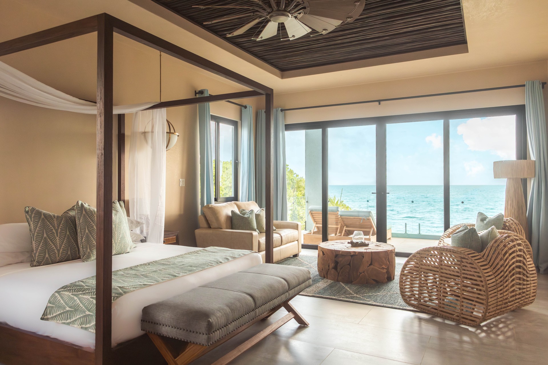 a room with a bed and chairs and a table with a view of the ocean
