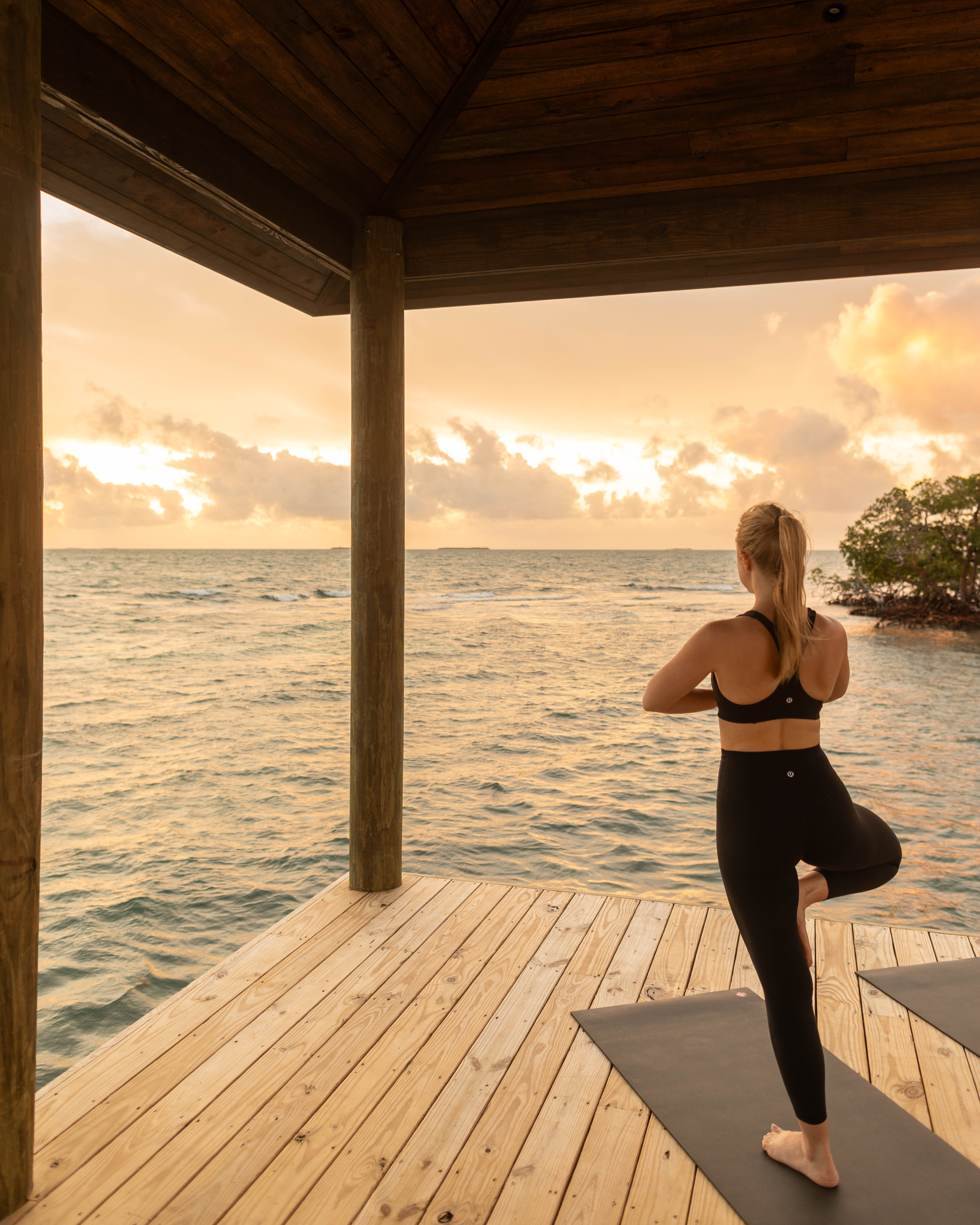a woman standing on one leg on yoga mat near water