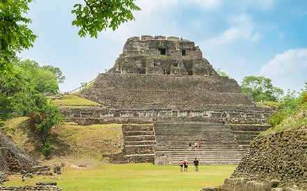 a group of people standing in front of a pyramid with Xunantunich in the background