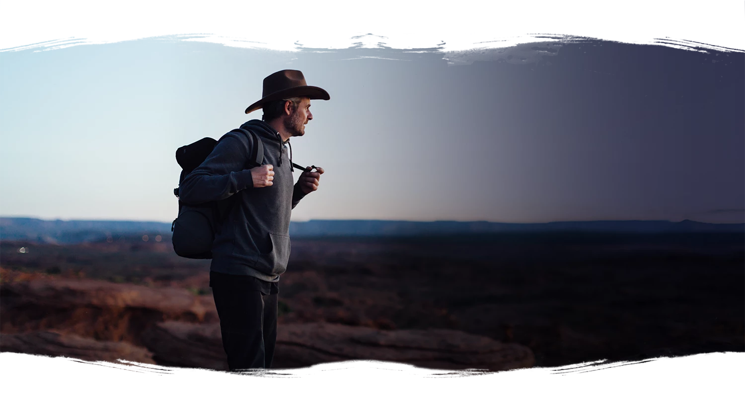 man in a cowboy hat hiking the open fields