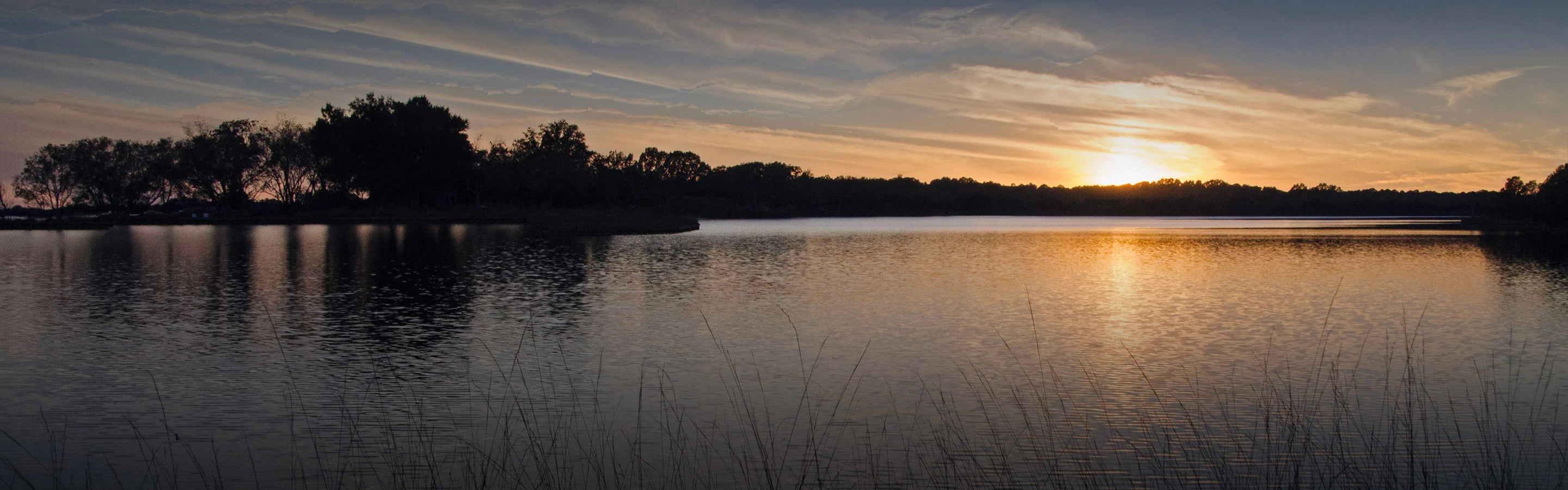 a body of water with trees and a sunset in the background
