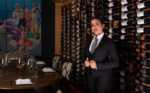 a woman in a suit standing in front of a wine rack