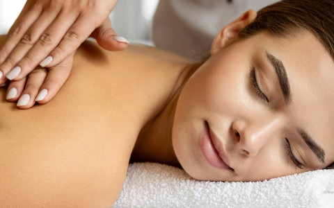 a woman lying down on a towel with her eyes closed getting a massage on her back