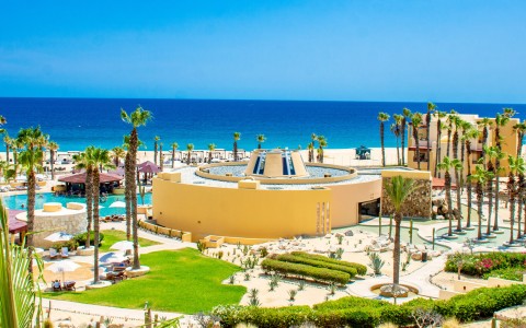 a building with a pool and palm trees on a beach