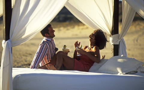 a man and woman sitting on a bed with drinks