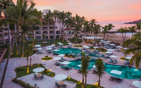 a pool and palm trees with a hotel and a beach