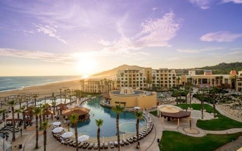 a pool with palm trees and buildings by the beach