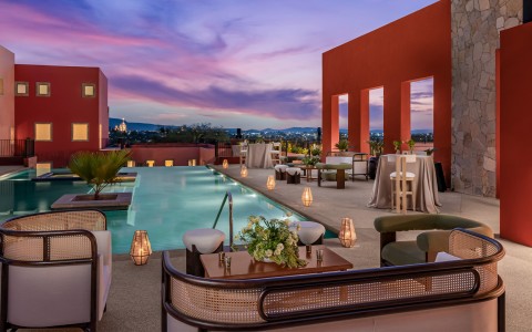 a pool with tables and chairs and a pink sky