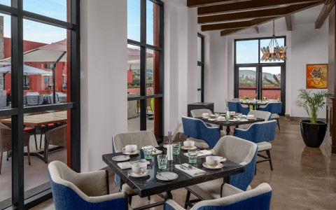 Bright restaurant dining room with blue chairs and large windows looking out to a patio