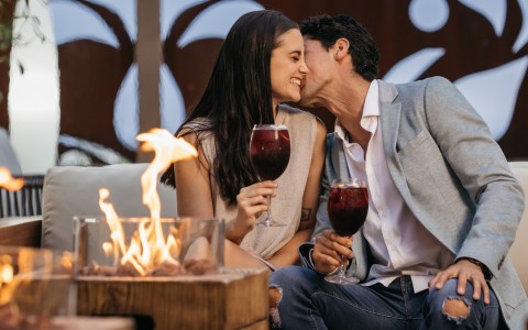 a man and woman holding wine glasses and kissing