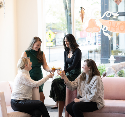 a group of women sitting on a couch and clinking glasses
