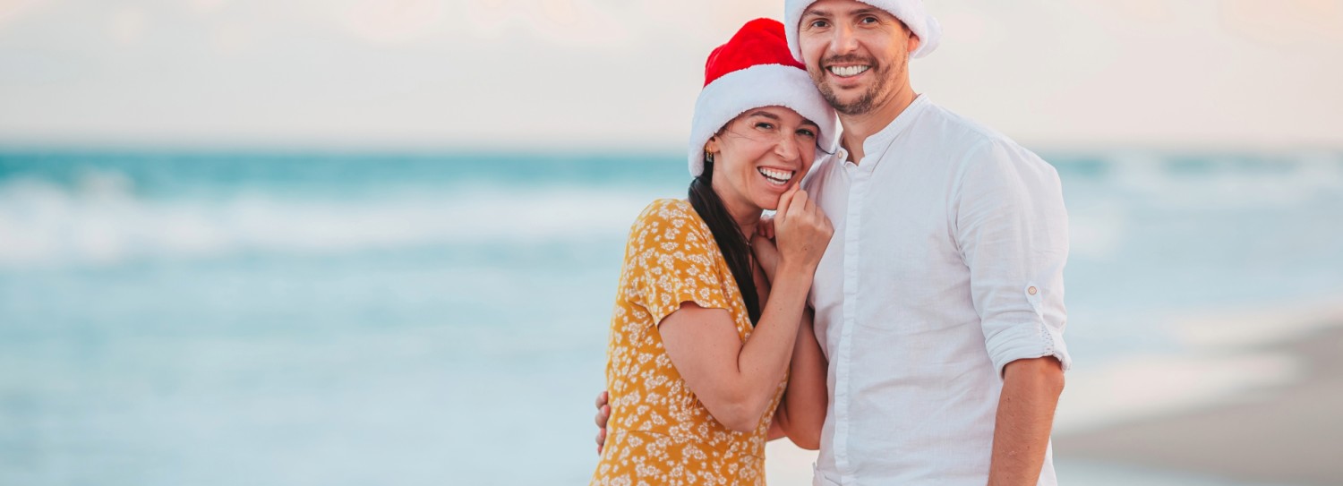 a man and woman wearing santa hats on a beach