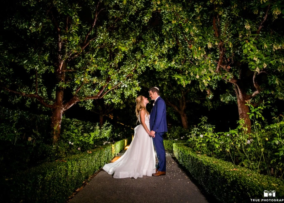 a man and woman kissing on a path in a garden