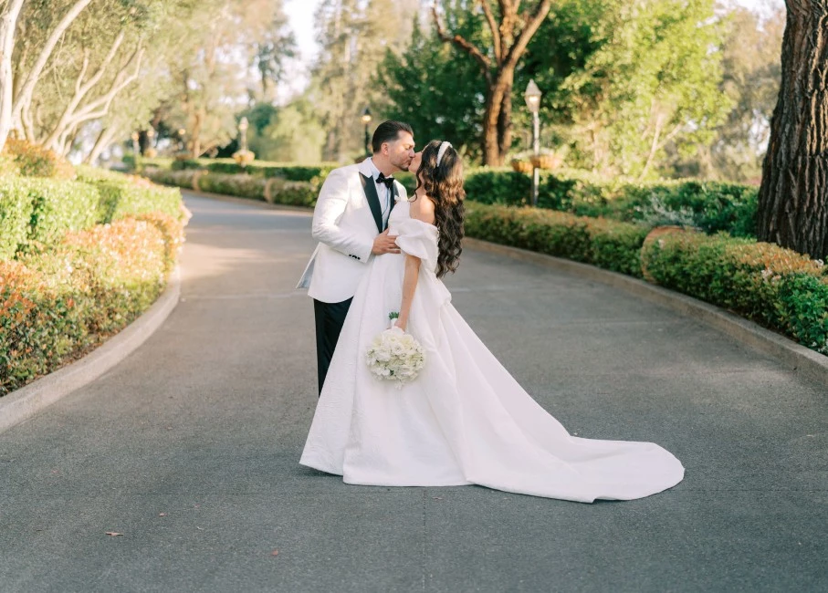 a man and woman kissing on a road with bushes and trees