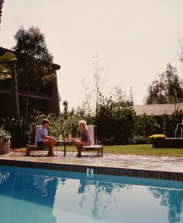 a man and woman sitting on a bench by a pool