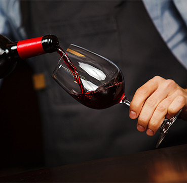 person pouring red wine into glass